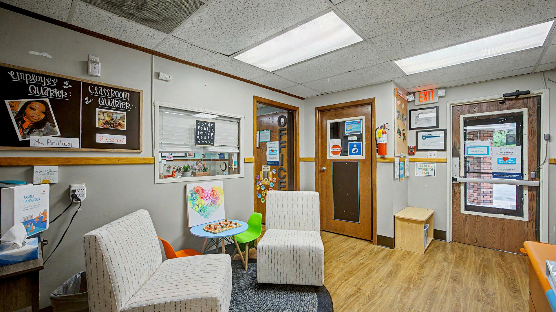 Lobby of a daycare with chairs, tables, and a classroom board