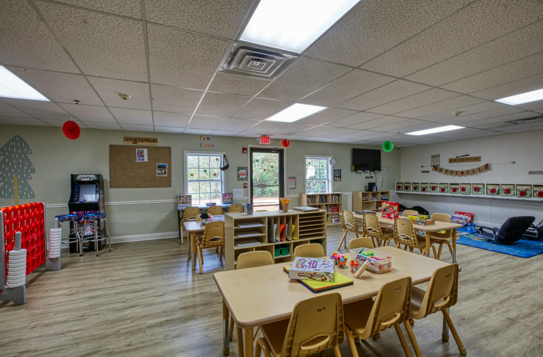 Classroom with small tables and chairs, shelves with books and supplies, an arcade game