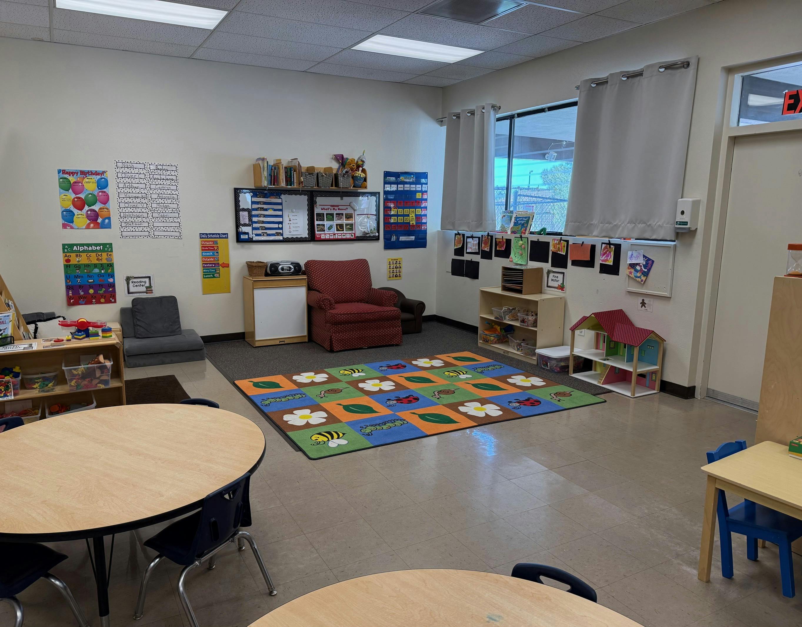 An empty early childhood classroom with tables, chairs, colorful rug, and posters
