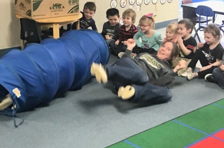 Person on floor with children watching another person in a blue tunnel