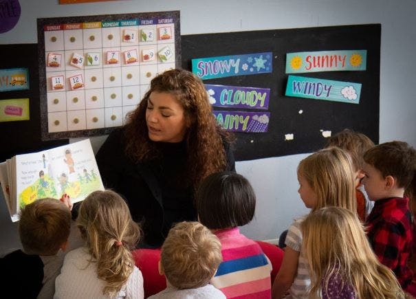 Person reading a book to a group of children in a classroom