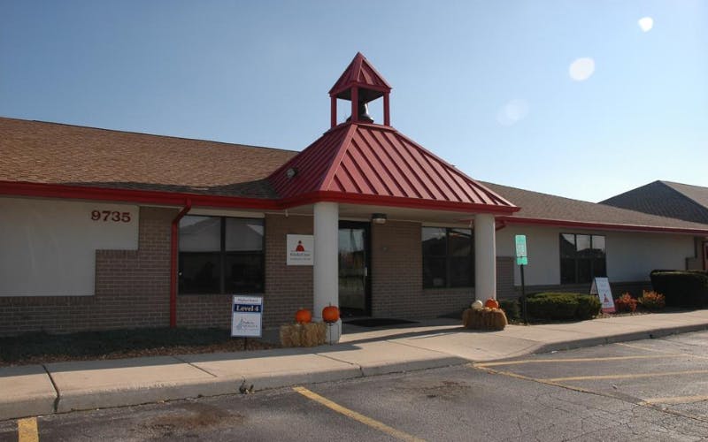 Building with 9735 on the side and a red roof over the entrance with a bell tower