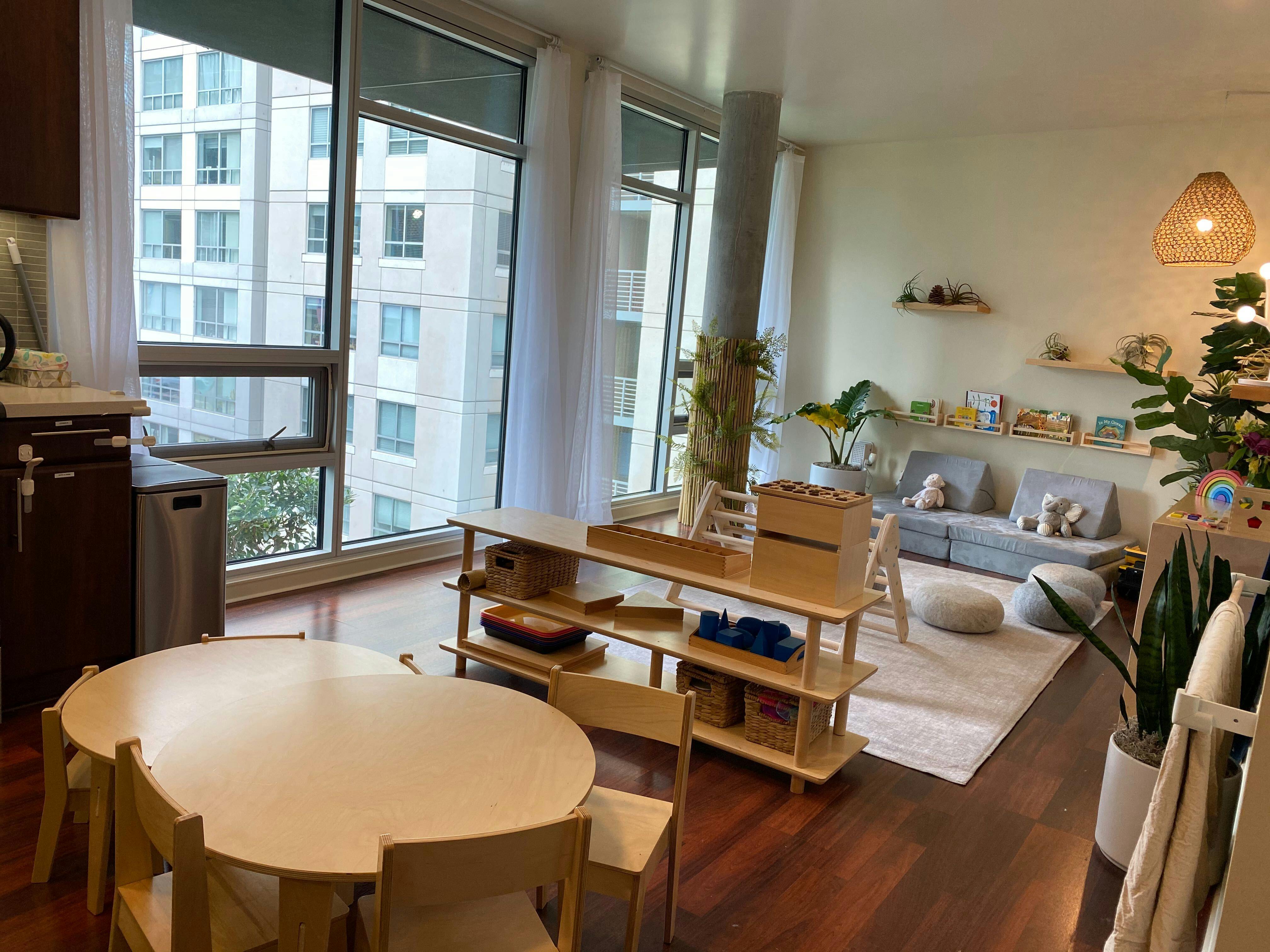 Children's play area with small tables and shelves, large windows overlooking buildings