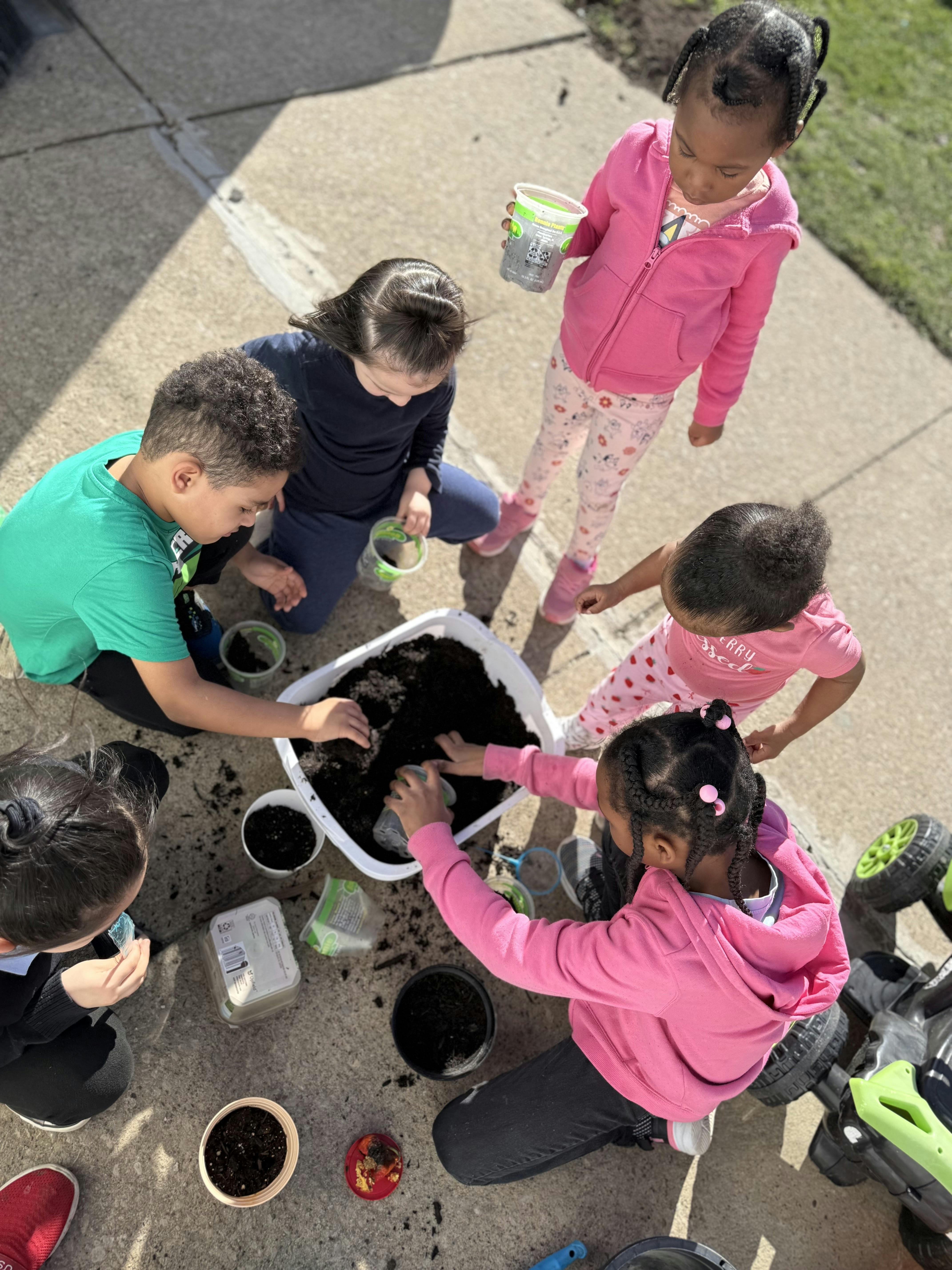 Five children planting in a large white container filled with soil