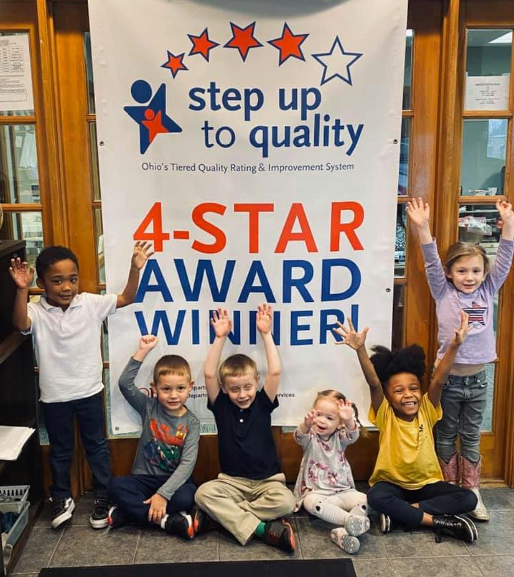 Children with hands raised in front of a "4-STAR AWARD WINNER" banner