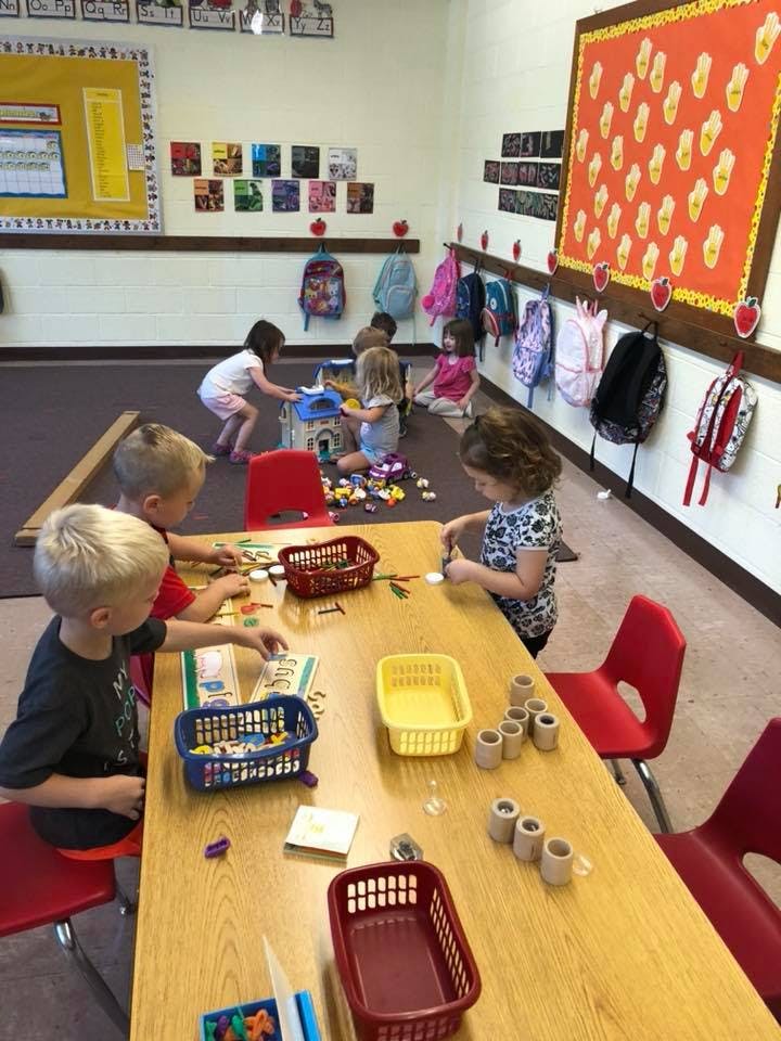 Children playing with toys at tables and on the floor in a classroom