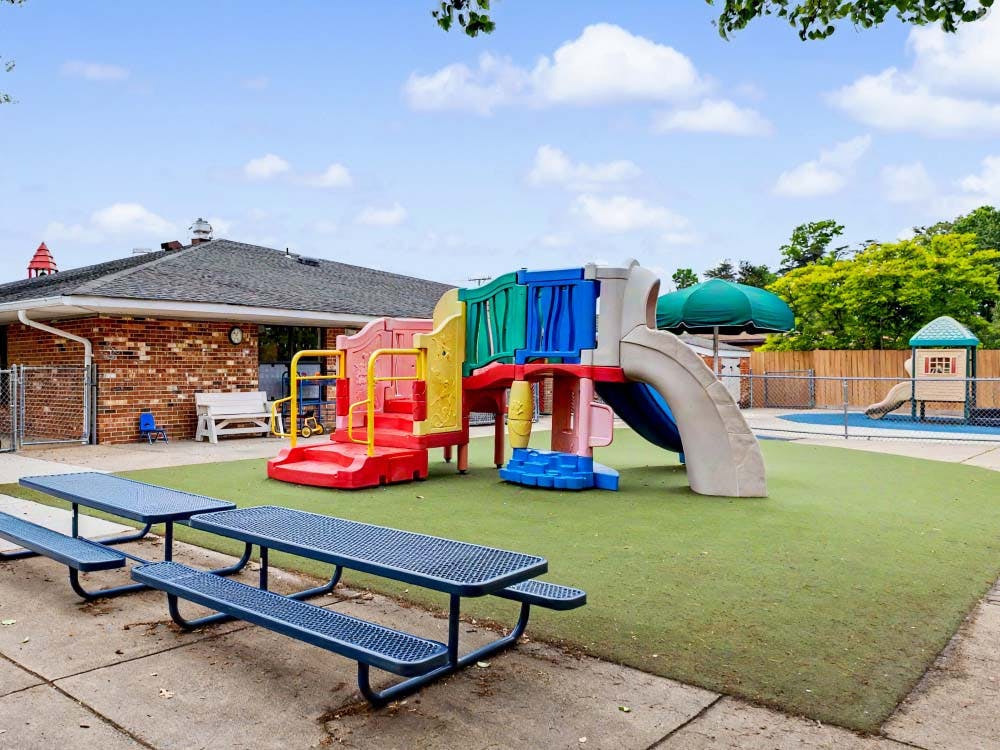 Colorful playground structure with slides on artificial turf next to a brick building