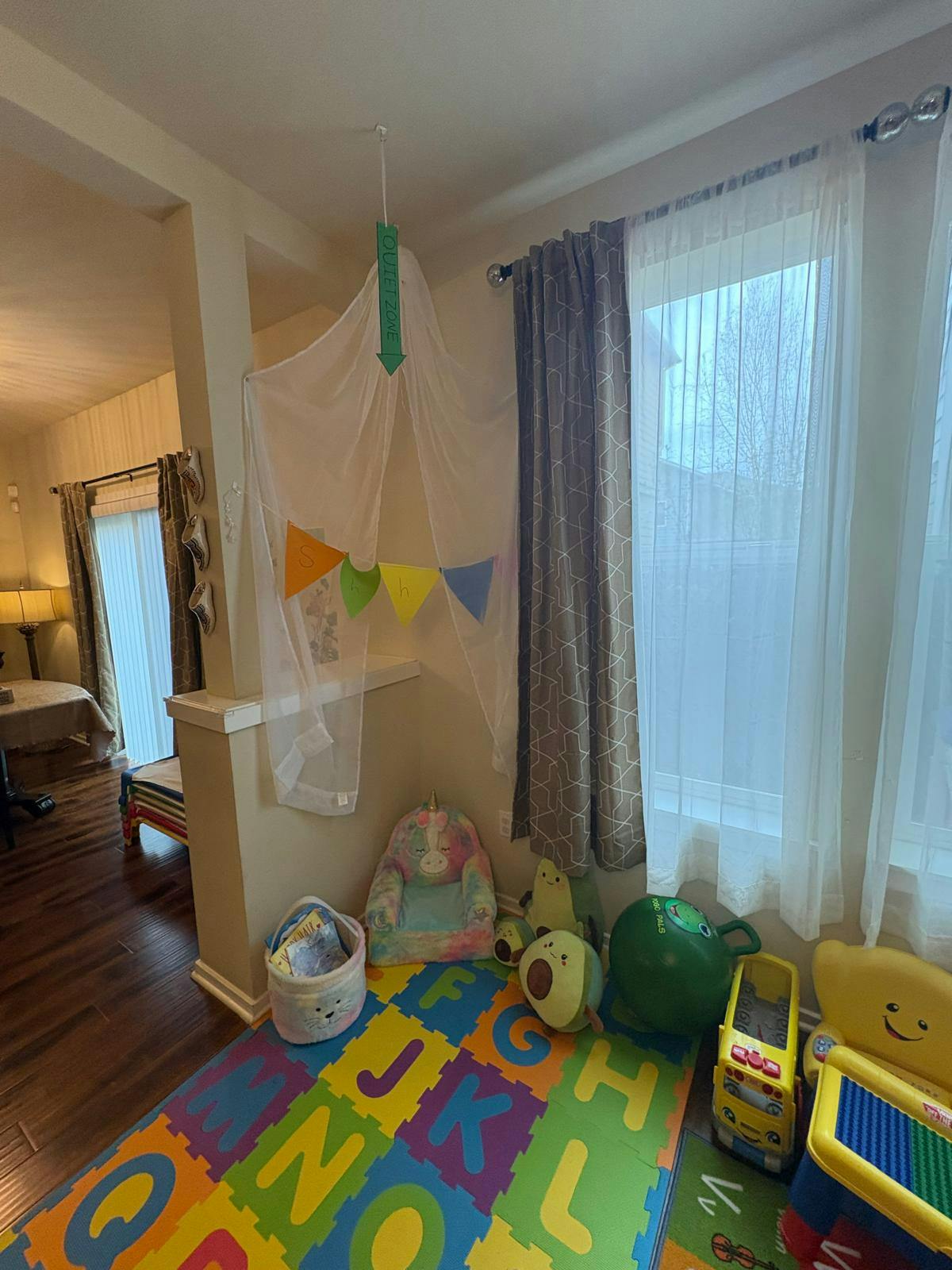 Play area with a colorful alphabet mat, toys, and a sheer canopy