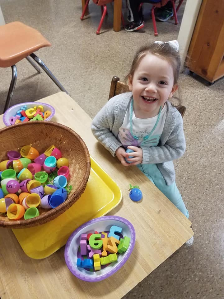 Child at a table with bowls of colorful plastic eggs and letter shapes