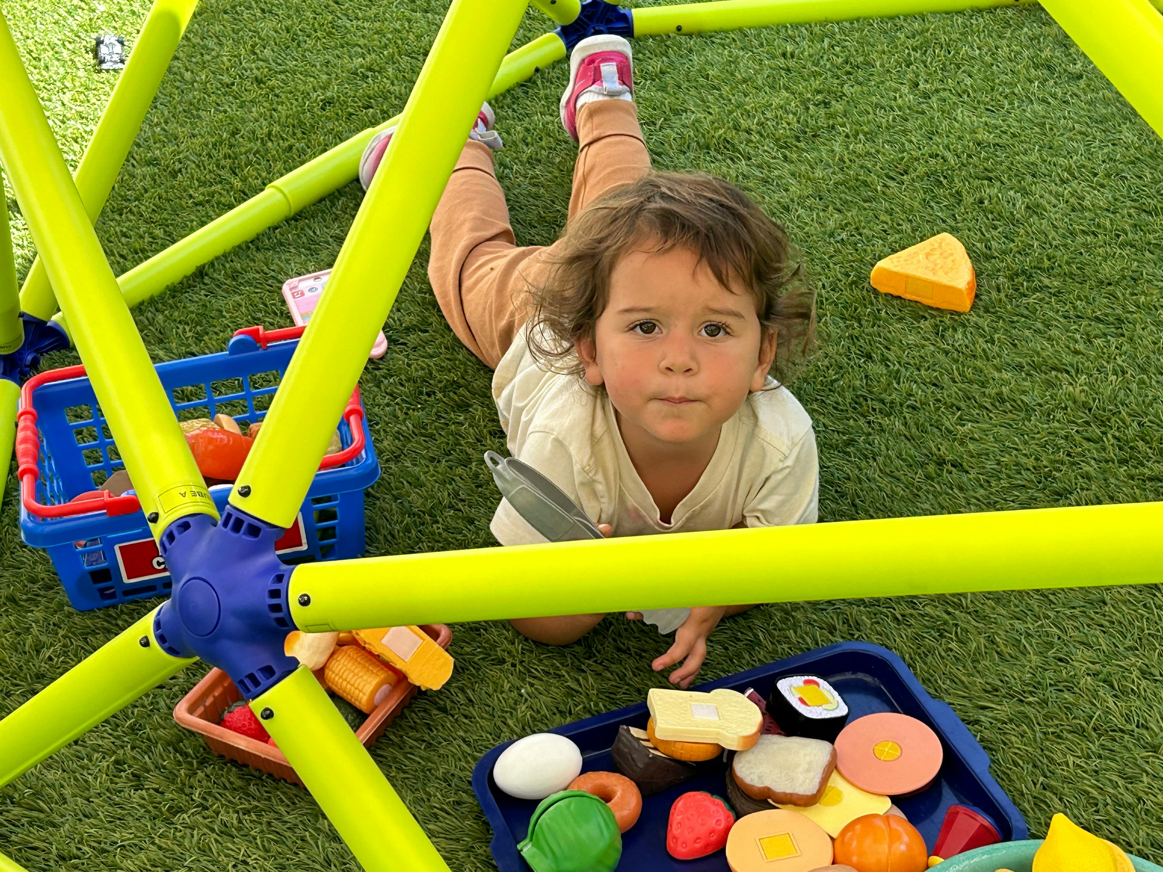 Child lying on green turf under a play structure with toy food