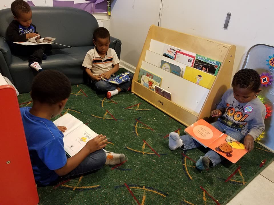 Four children reading books in a classroom