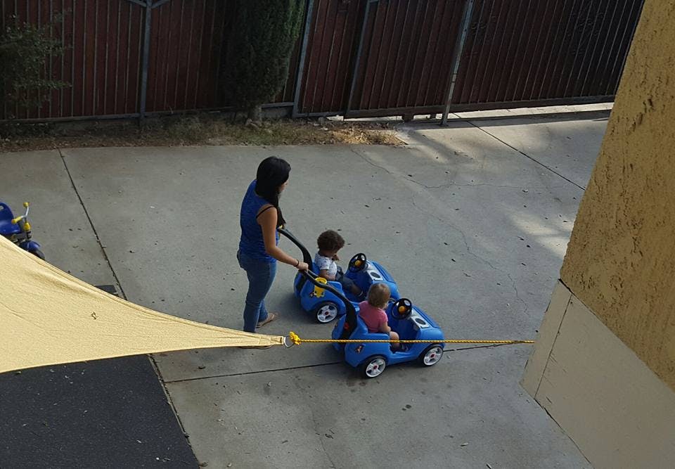 Person pushing two children in toy cars