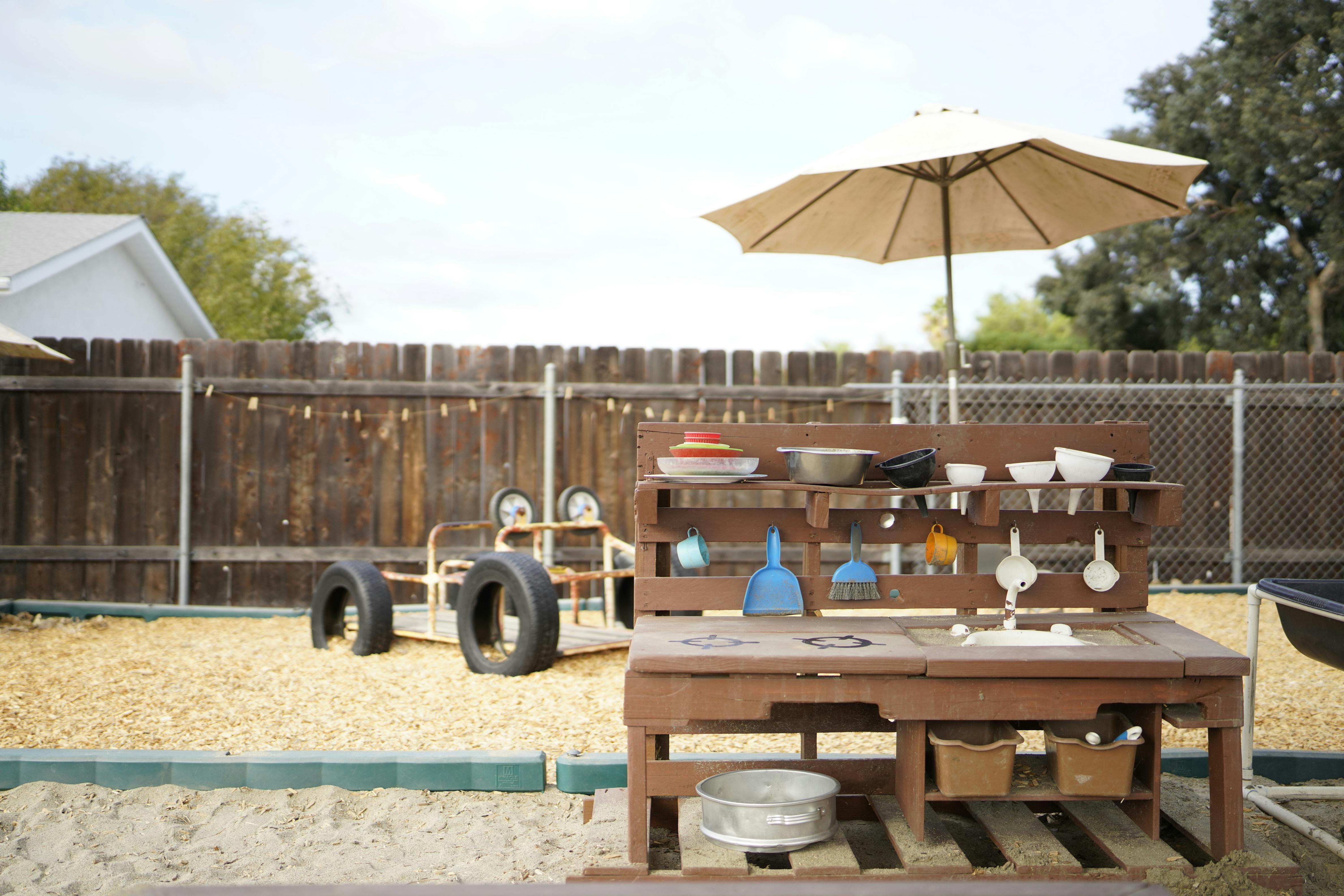 Outdoor play kitchen with an umbrella and toy car in a fenced yard