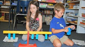 Two children playing with a balance scale on the floor