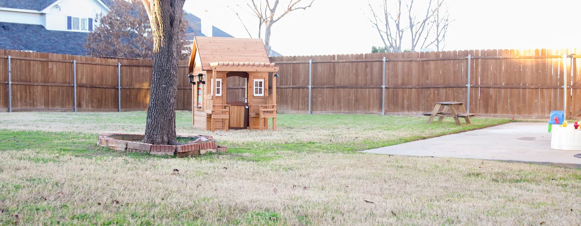 Backyard with a wooden playhouse, tree, and picnic table