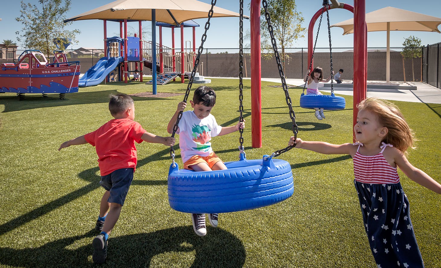 Three children playing on swings and a playground