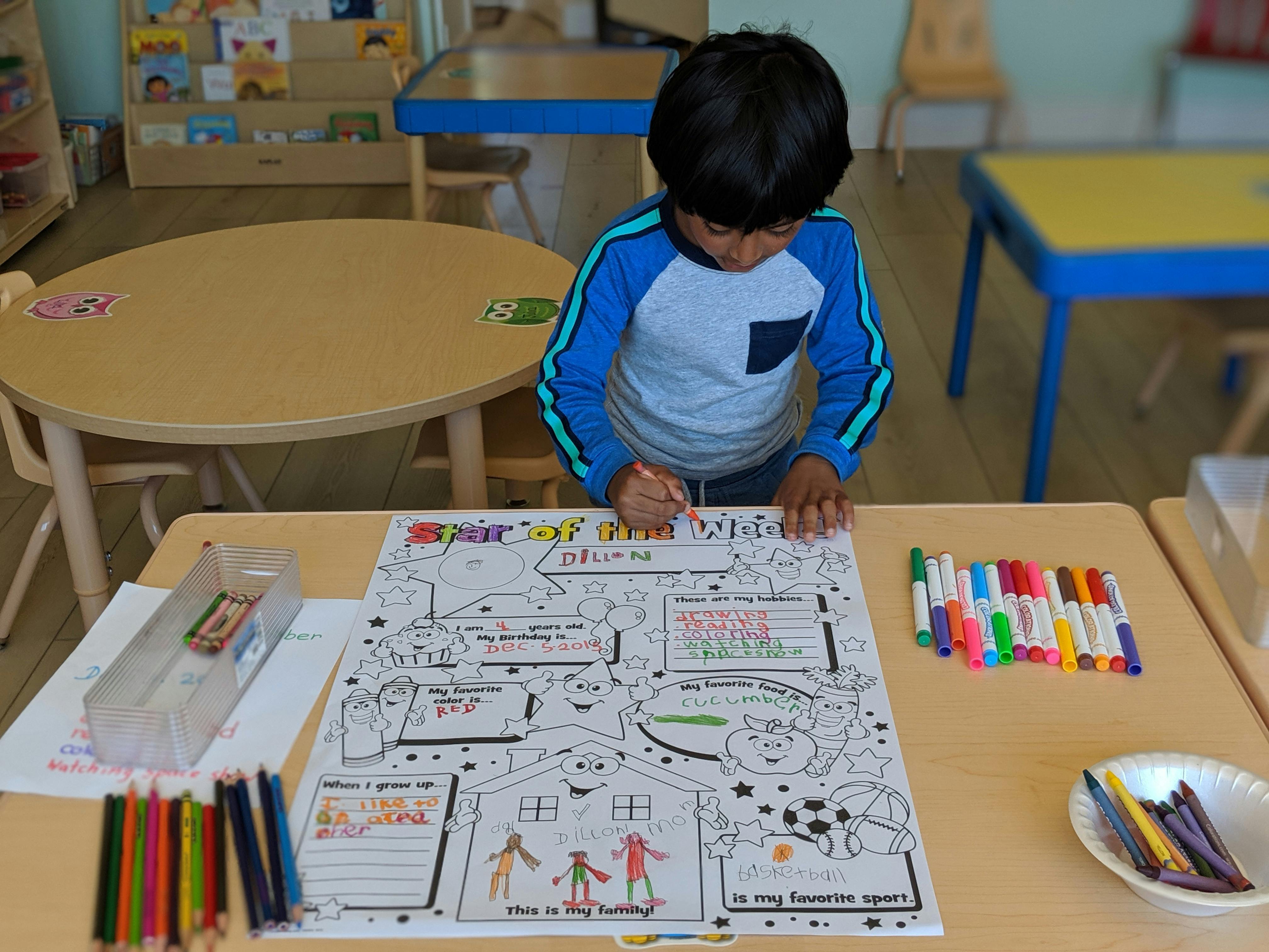 Child coloring a large paper with markers at a table