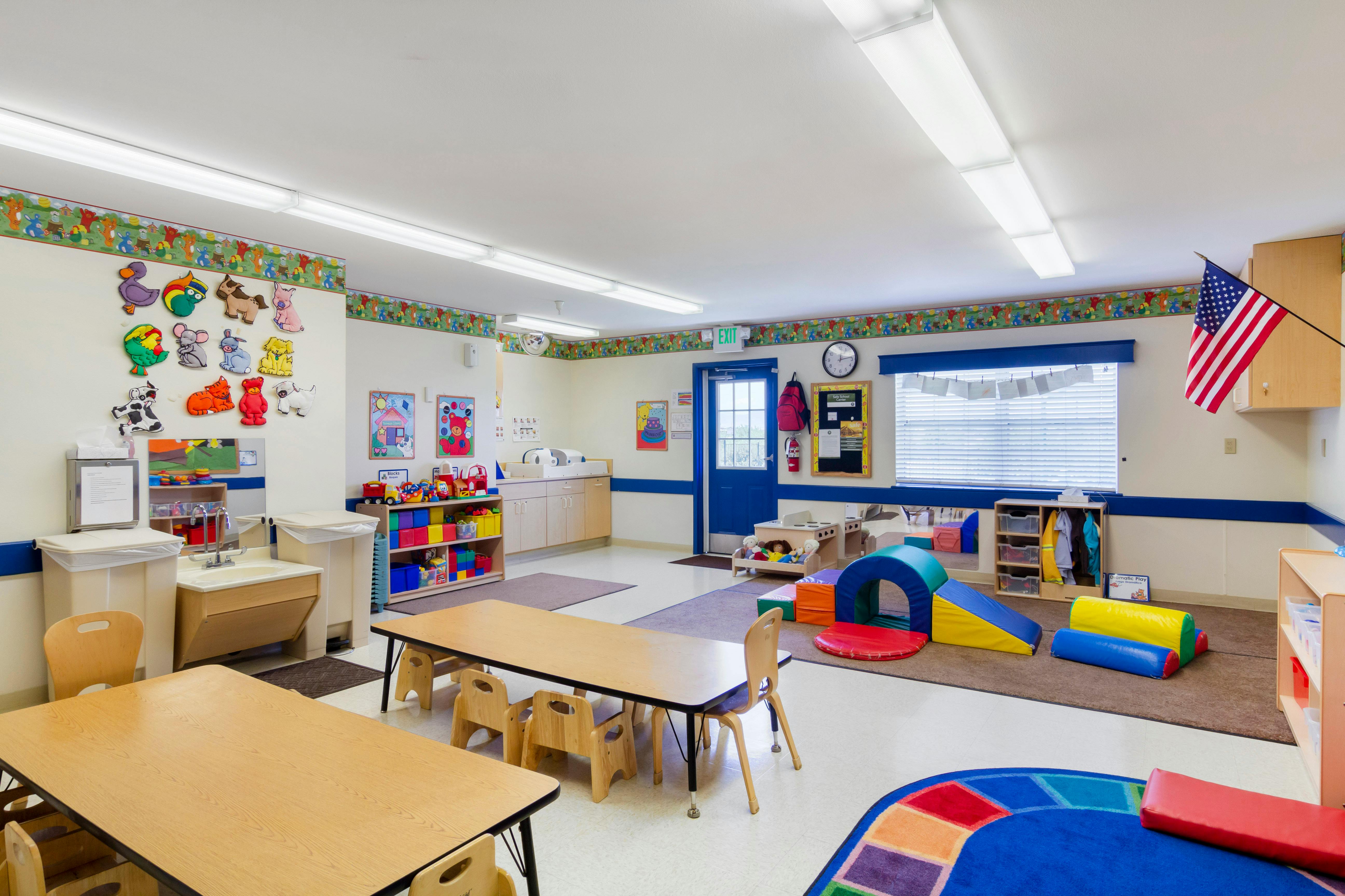 A children's classroom with small tables, chairs, and play equipment