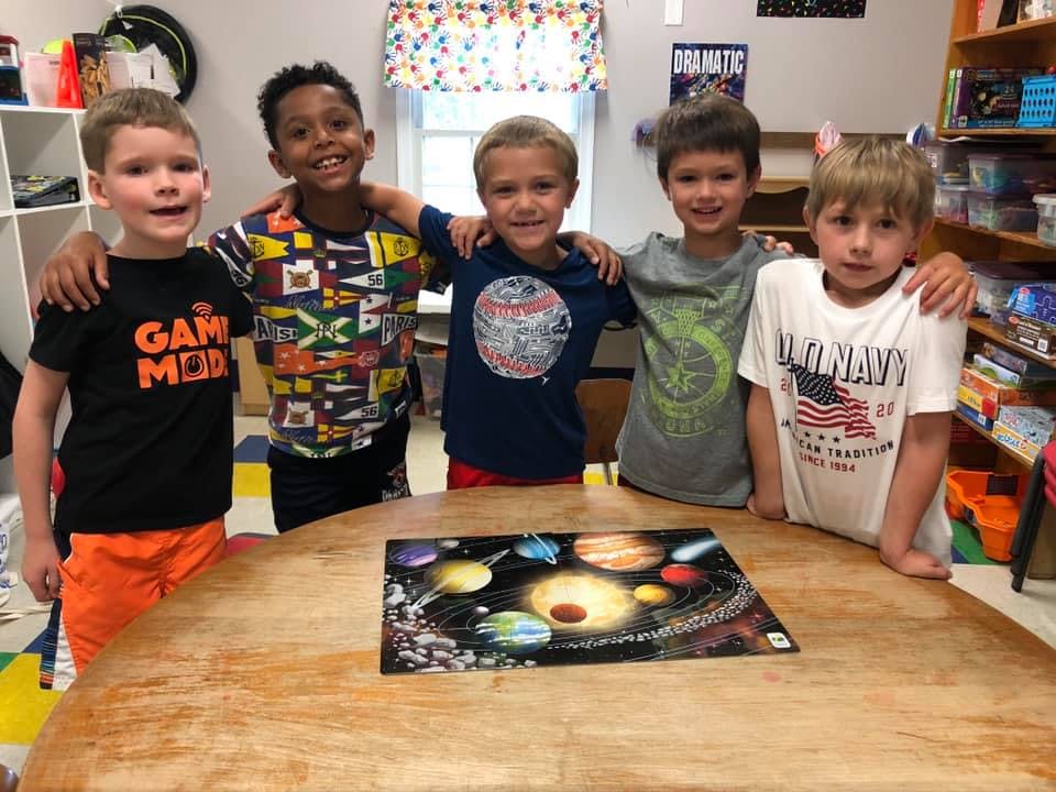Five children standing around a table with a solar system puzzle