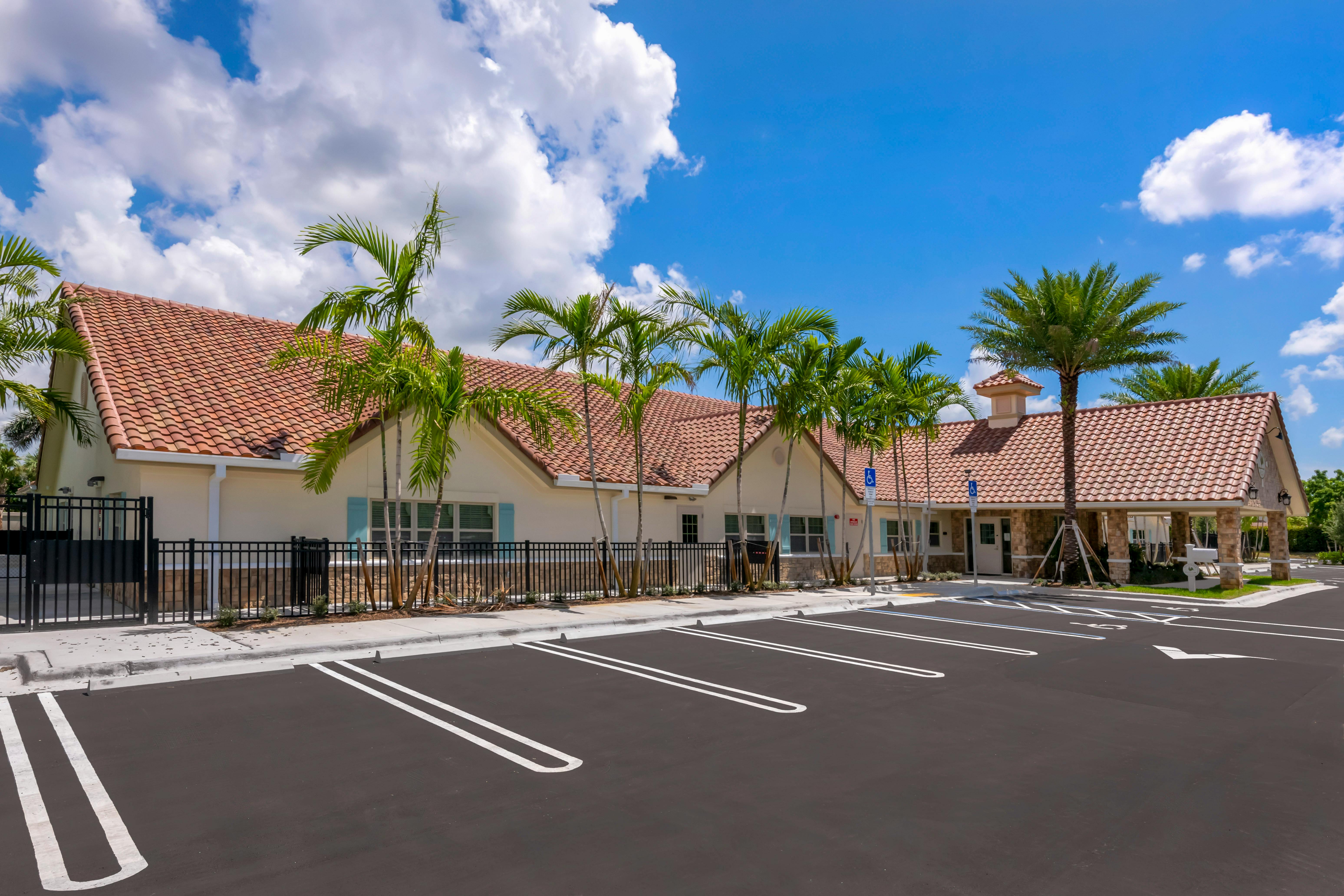 A beige building with a red tiled roof and palm trees outside