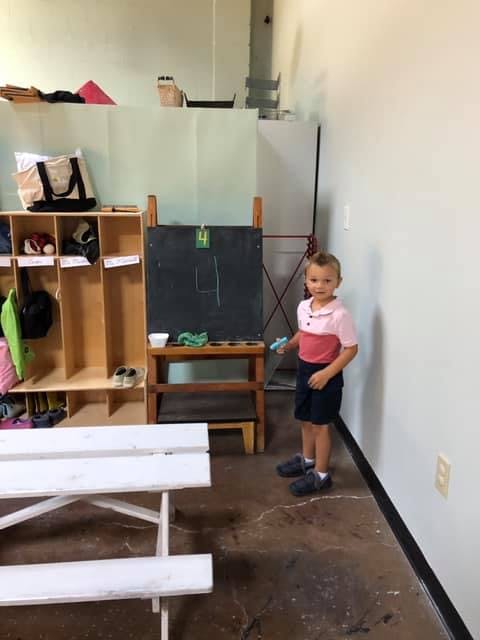 Child standing next to a chalkboard easel in a classroom
