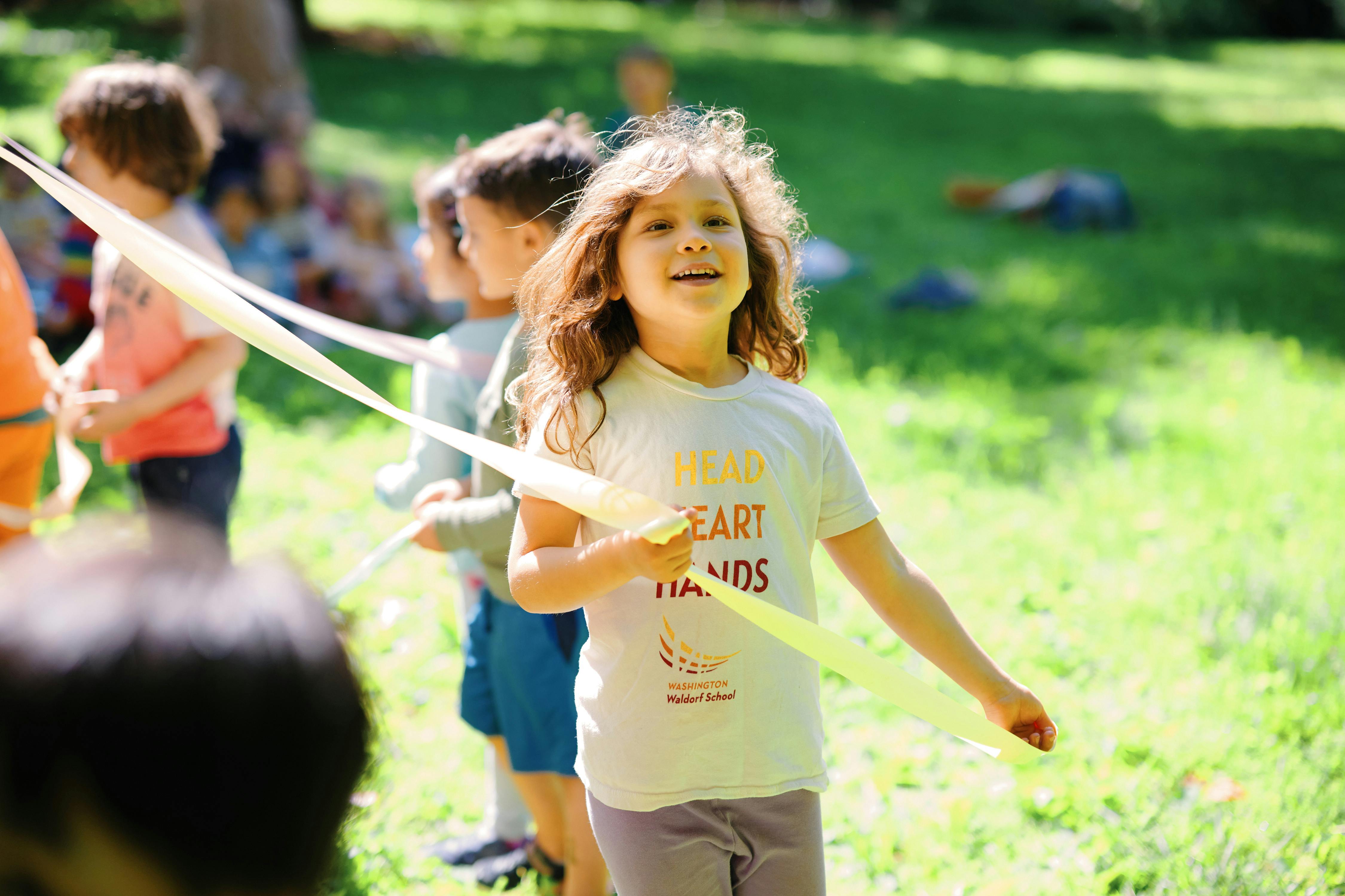 Child holding a yellow ribbon with other children in a line outdoors setting with grassy area