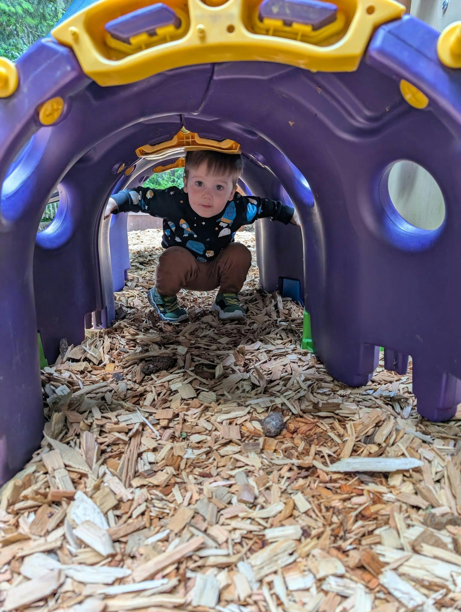 Child crouching in a purple and yellow play tunnel on a playground