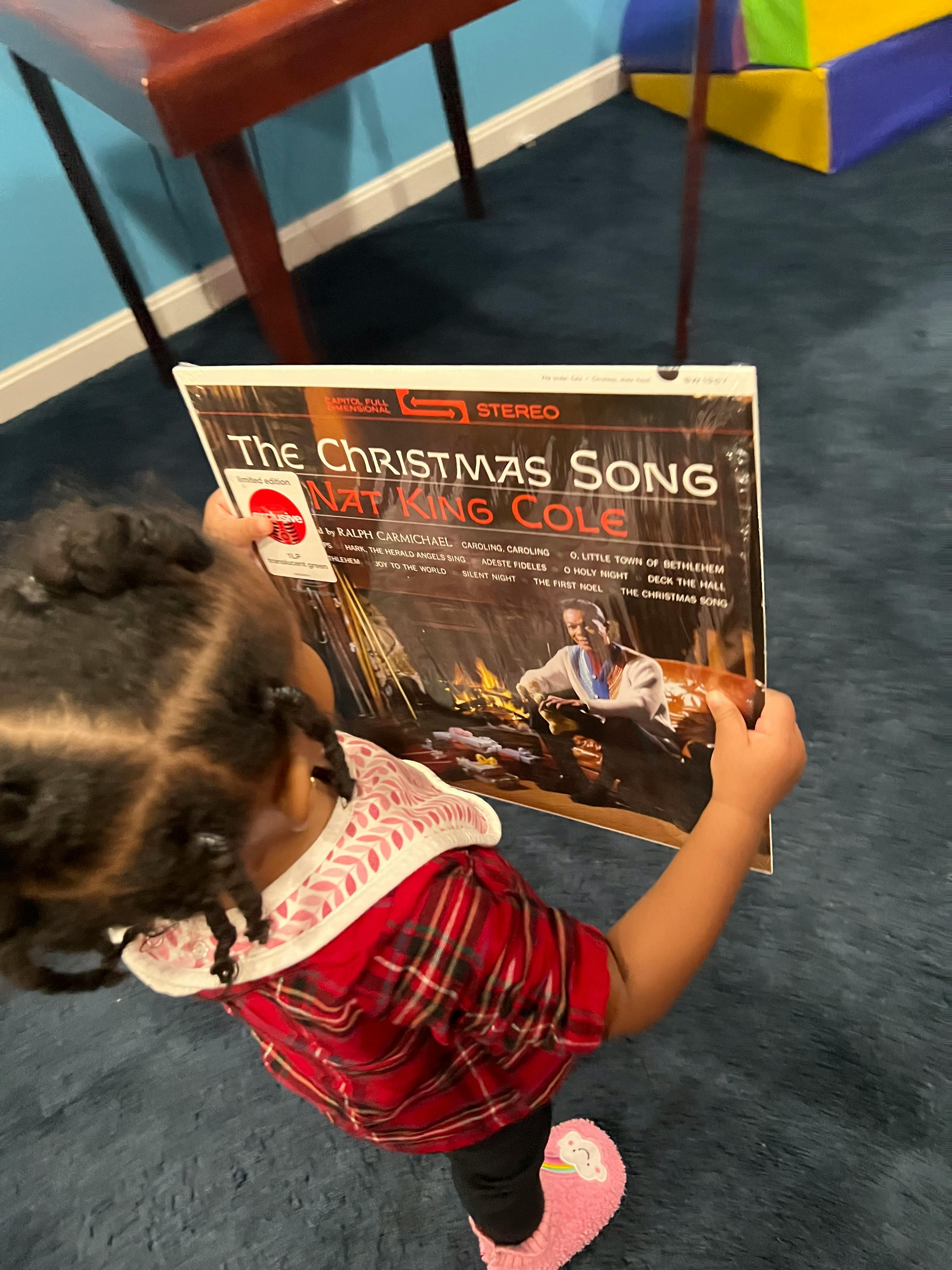 Child holding a record album titled "The Christmas Song" by Nat King Cole