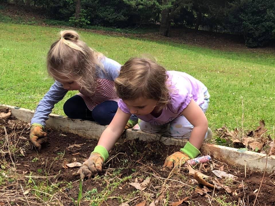 Two children in gloves planting in a garden bed