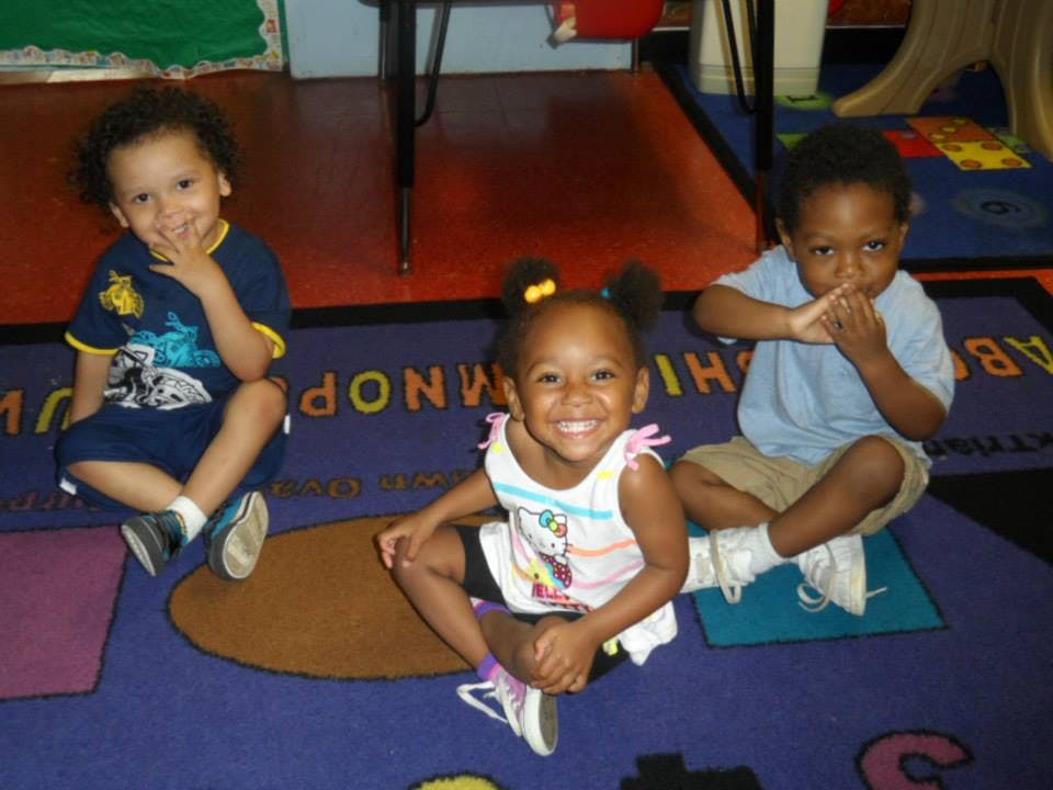 Three children sitting on a rug with alphabet letters