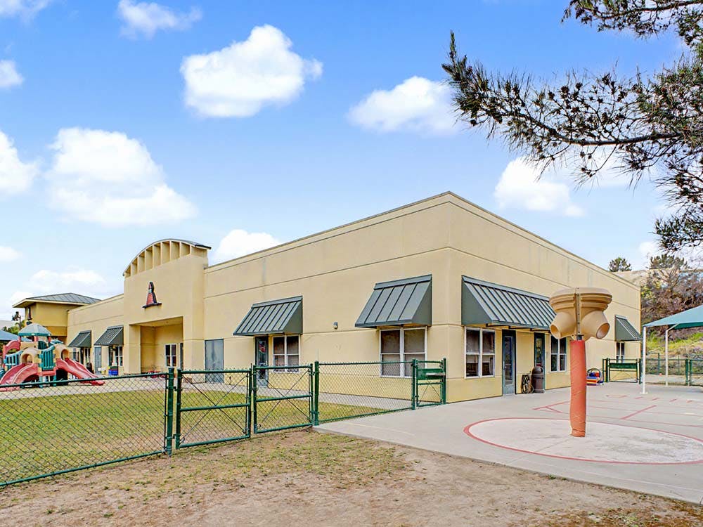 A beige building with green awnings next to a playground area and grassy yard