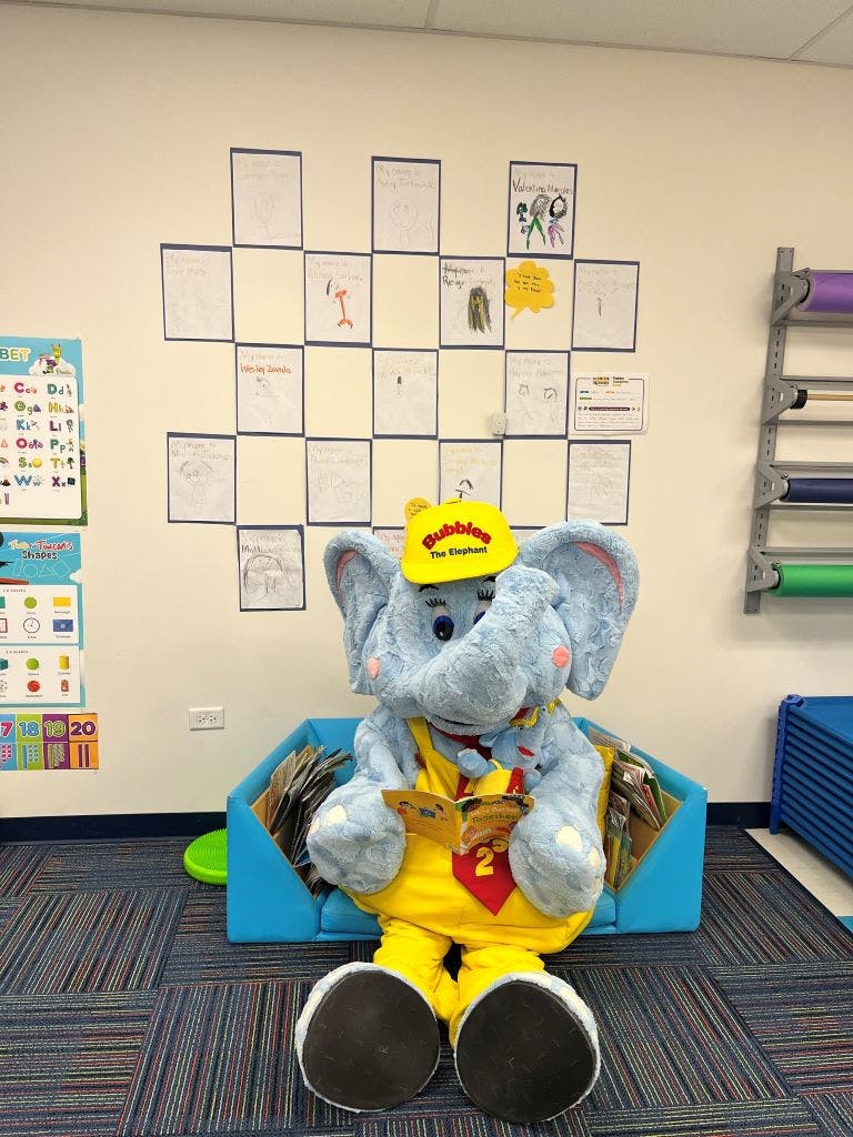 Elephant mascot in yellow hat and overalls reading a book