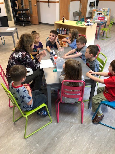 Adult and children gathered around a table in a classroom