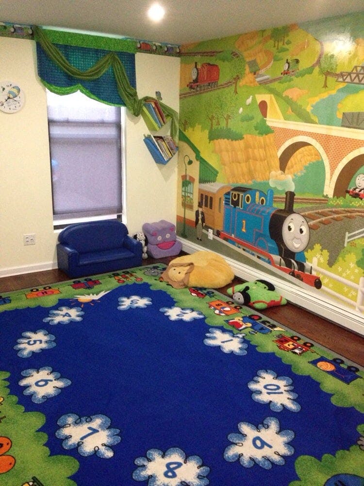 Playroom with a blue rug, small blue couch, and a train mural on the wall