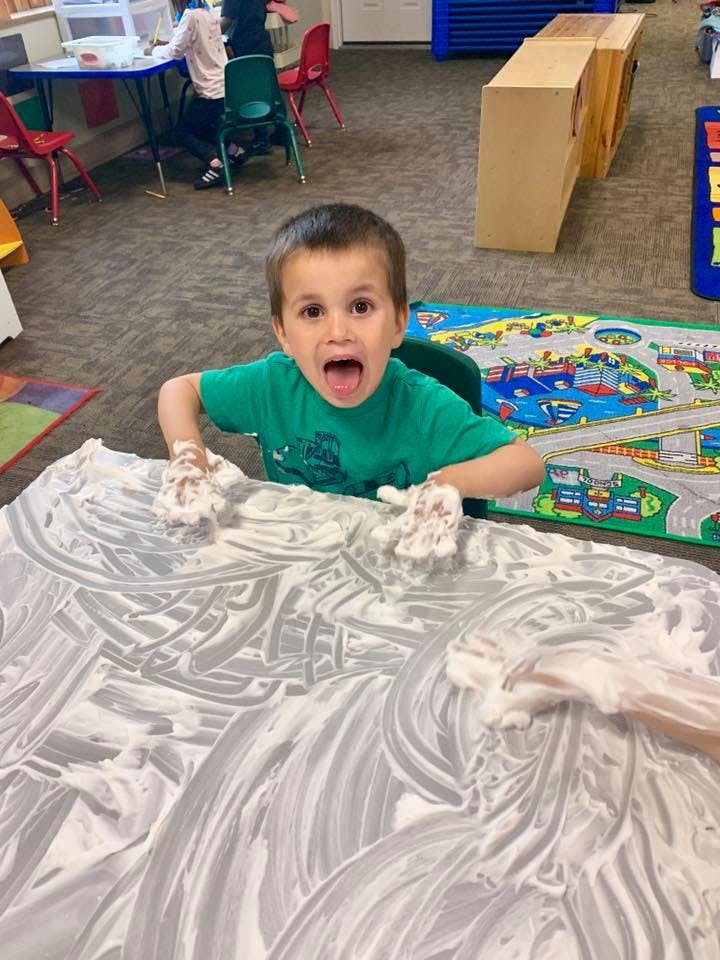 Child with hands covered in shaving cream at a table