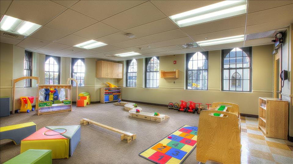A classroom with playmats, toys, and large arched windows