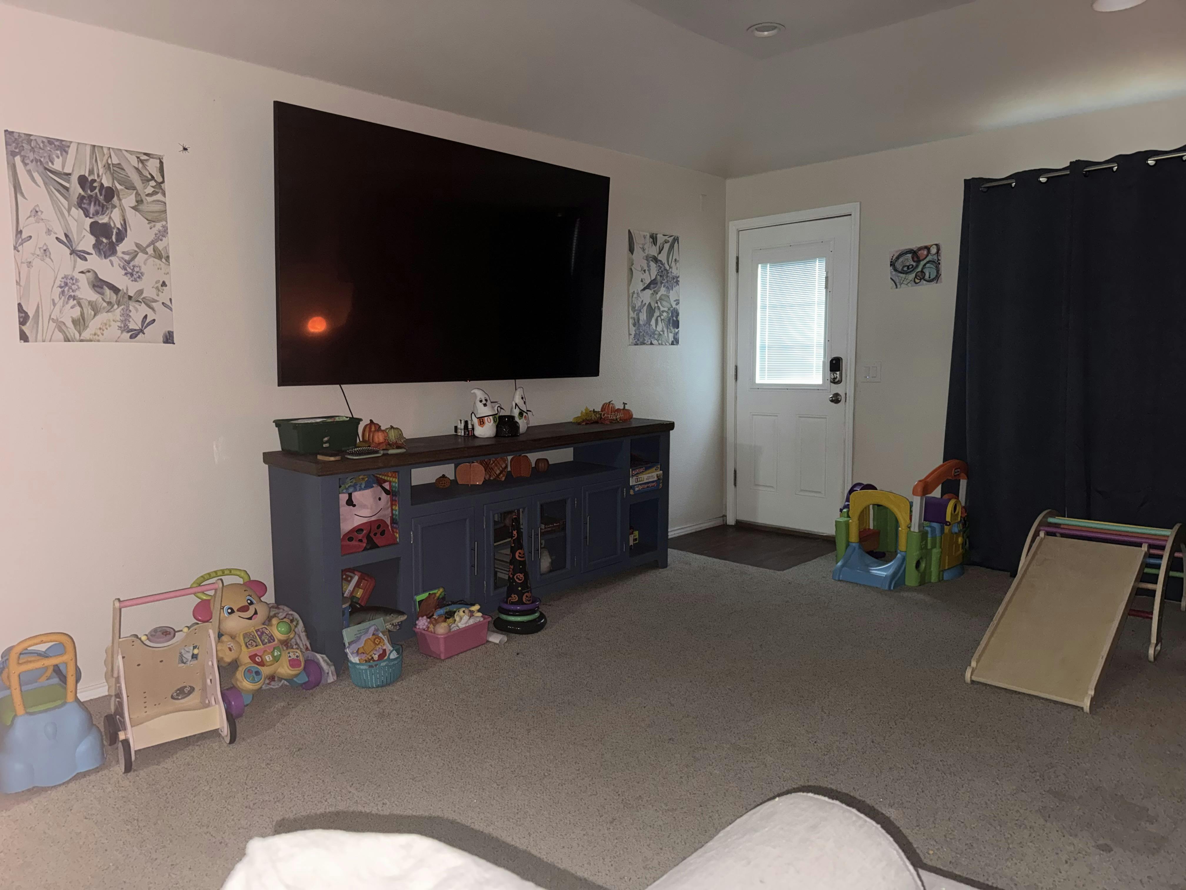 Living room with a large TV, entertainment console, and children's toys