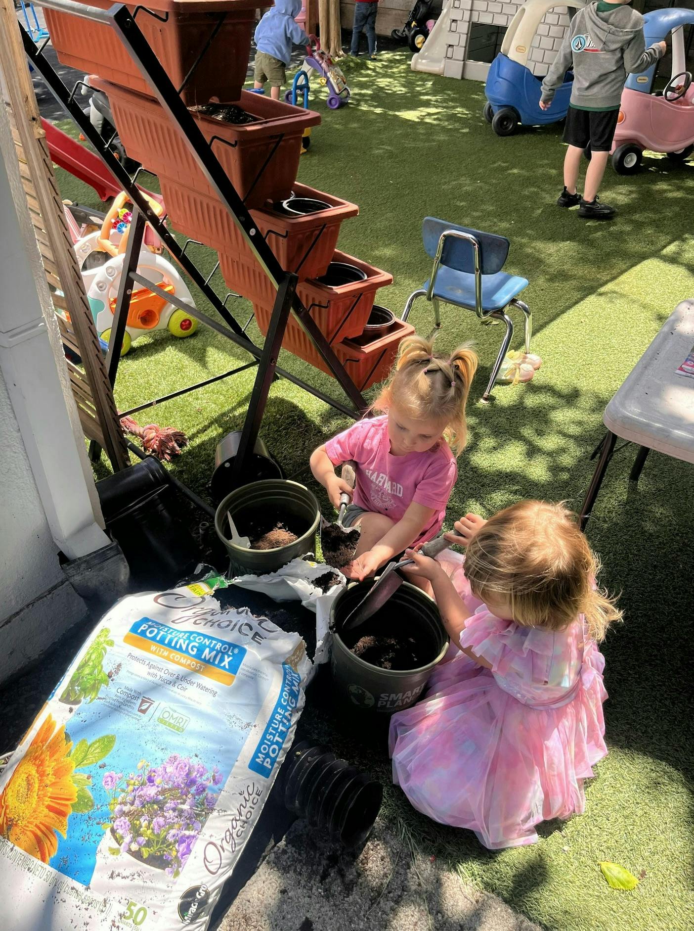Two children playing with potting mix and buckets