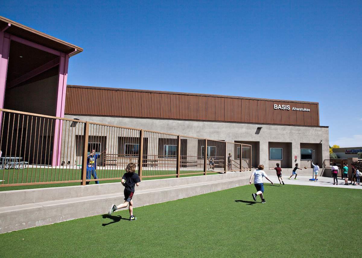 Children playing on a grassy field in front of a school building with a sign that reads BASIS Ahwatukee