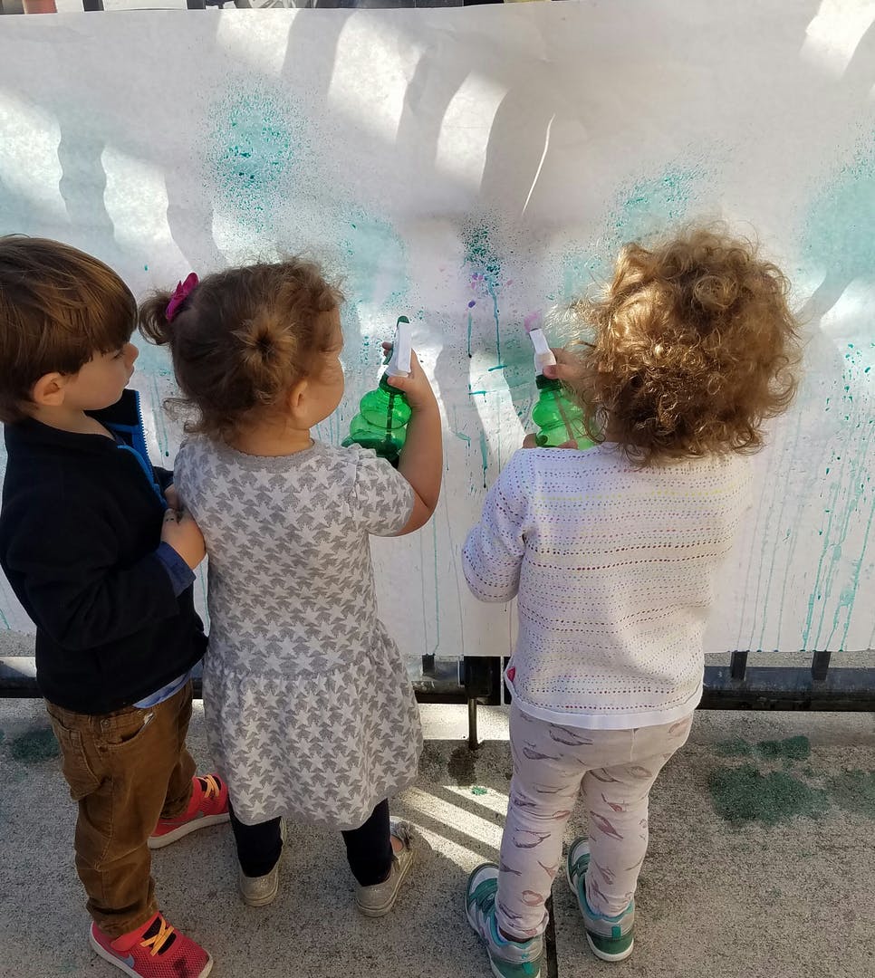 Three children spraying a white surface with bottles