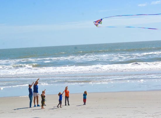 People and children flying a kite on a beach