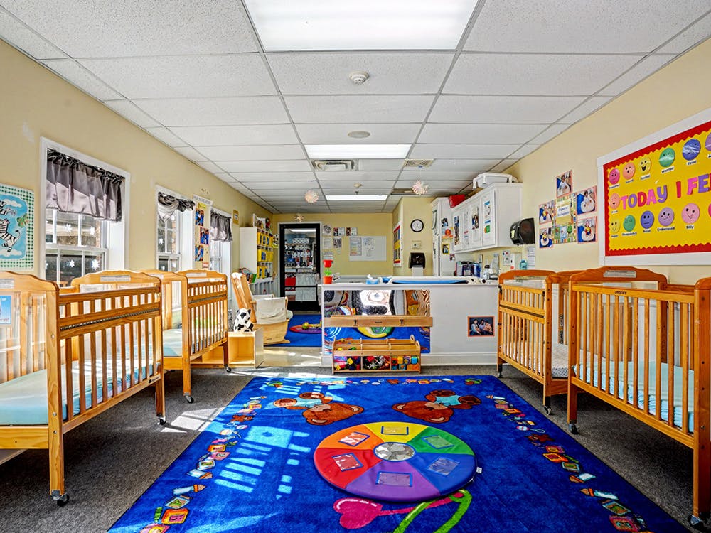 Cribs inside a daycare room with a colorful play rug