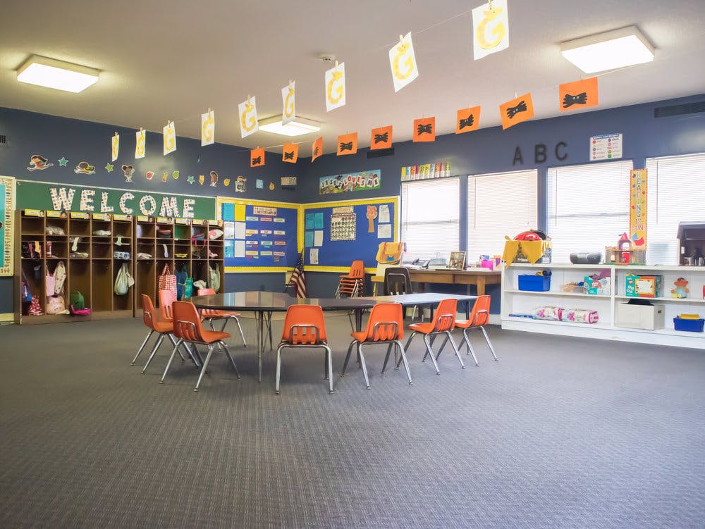 Empty classroom with small tables and orange chairs, cubbies, and bulletin boards