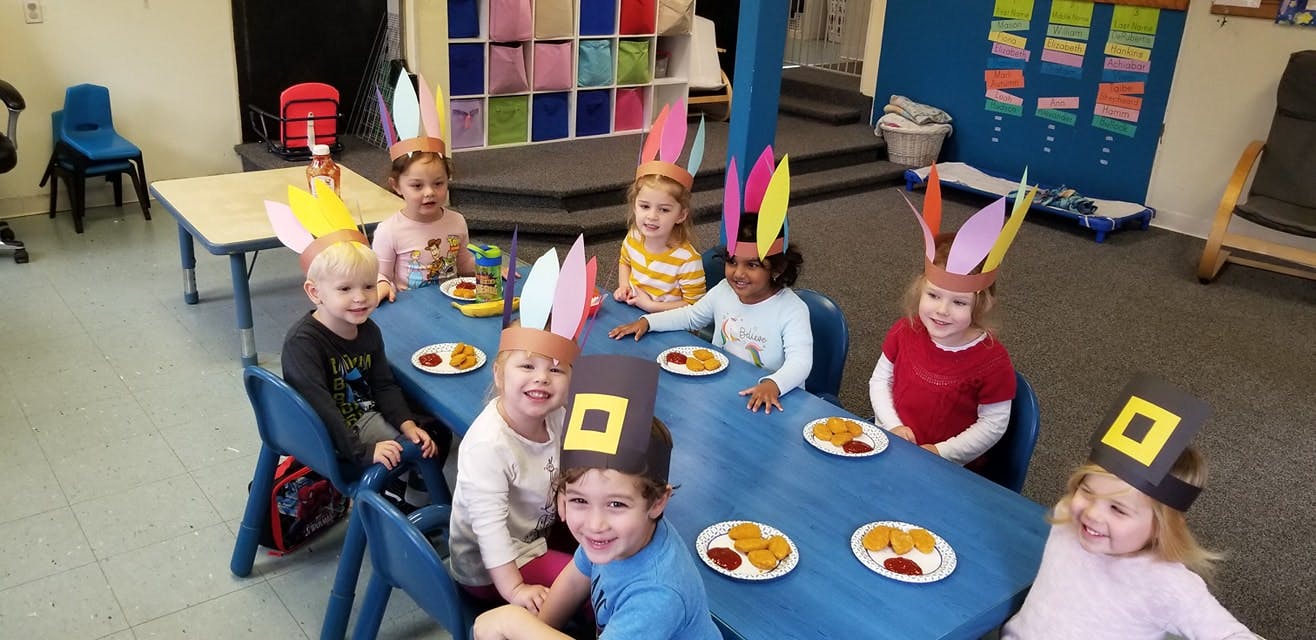 Children wearing bunny ears and pilgrim hats sitting at a table with food