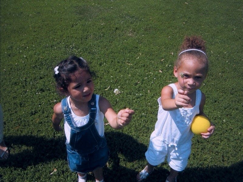 Two children on grass, one holding a yellow ball and pointing