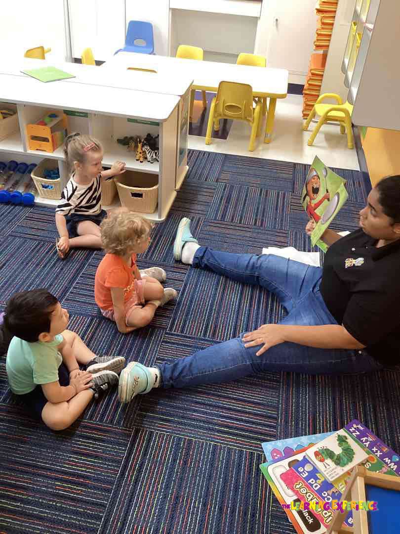 Adult reading a book to three children in a classroom