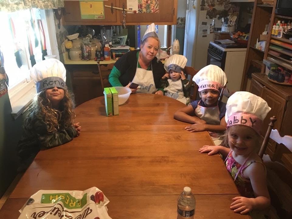 Adult and children wearing chef hats and aprons around a table