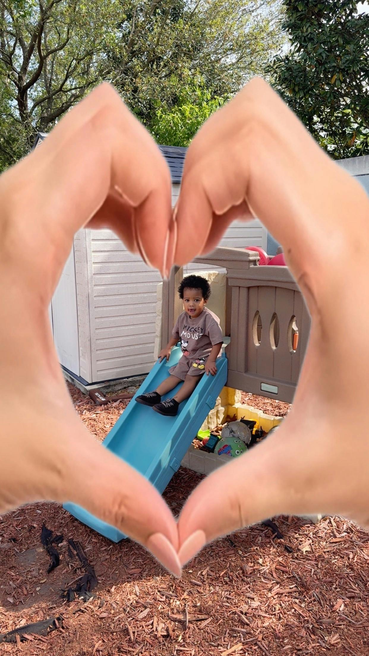 Child sitting on a slide framed by hands shaped into a heart