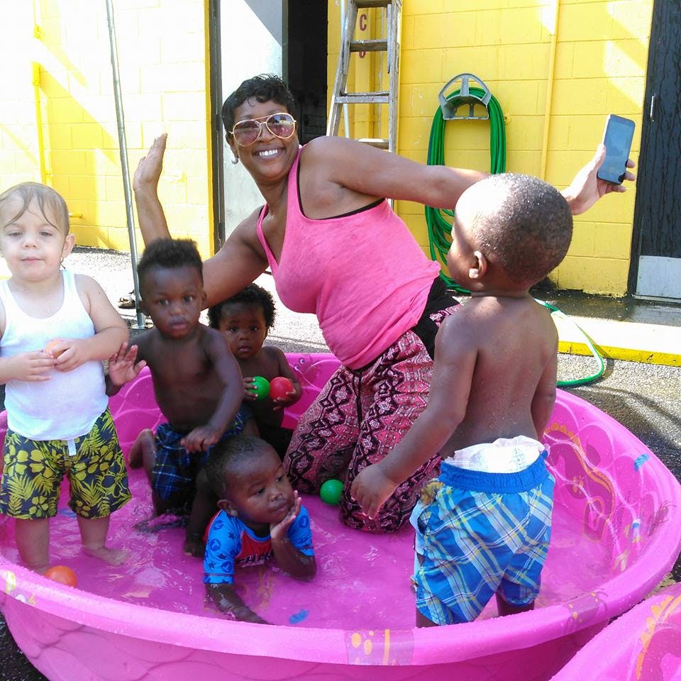 Adult and multiple children playing in a pink wading pool