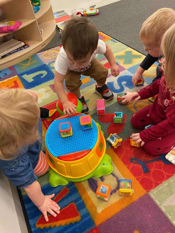 Children playing with blocks and a turtle toy on a colorful rug